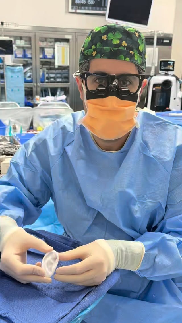 Dr. Tahiri in surgical attire holding an ear implant in the operating room